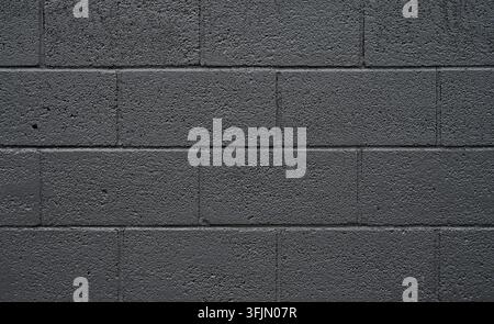 Dark gray painted cinder block masonry in a close-up horizontal view, with rough concrete faces, recessed cracked mortar joints Stock Photo