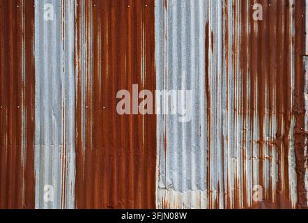 Distressed corrugated galvanized metal siding with vertical ridges, heavy iron-oxide rust, a ridge crushed from top to bottom, dented panels Stock Photo