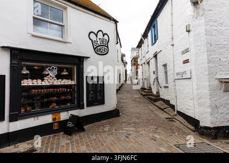 Traditional narrow streets and stone buildings in the historic centre of St Ives, Cornwall, England, with colourful bunting overhead and independent Stock Photo