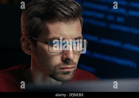 Portrait of a male software engineer stares with deep focus, working on a cybersecurity or machine learning project late at night programming script reflects in his glasses. Space for text Stock Photo