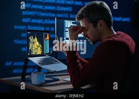 Fatigued developer removing eyeglasses and rubbing sore eyes during intense night programming work caused by blue light and prolonged screen time. Overworked coder facing burnout at computer desk Stock Photo