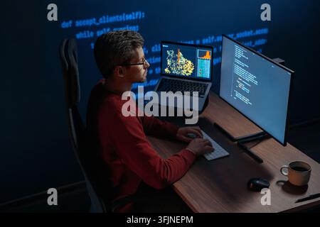 Concentrated data scientist typing code in a dimly lit workspace, multiple screens filled with programming code and data. Focused developer works late at night on a machine learning and ai project.  Stock Photo