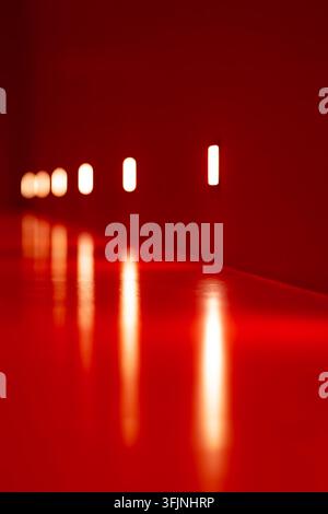 Minimalist surreal interior bathed in intense red light, with a rhythmic sequence of glowing white lamps and elongated reflections creating an abstrac Stock Photo