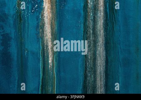 Abstract macro texture of a weathered, deep blue wall showing vertical streaks of water damage, white mineral deposits, and subtle peeling plaster. Ho Stock Photo