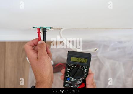 Person checks electrical wires in a wall with a digital multimeter during home renovation. Testing voltage before electrical installation or repair. Stock Photo