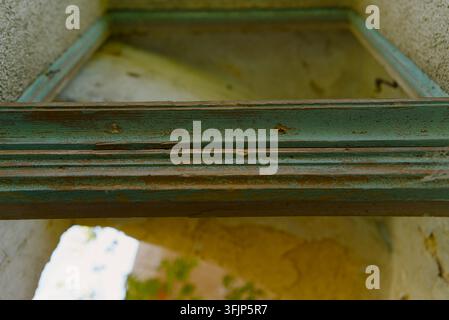 Close-up of an old, weathered wooden window frame with peeling green paint in an abandoned building. Stock Photo