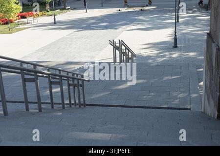 Broad stone steps with metal handrails lead into a paved public square in Eger, Hungary. Trees, flower beds, ornate street lamps, and distant pedestri Stock Photo