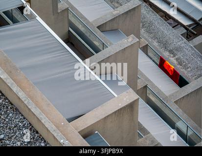 Abstract high-angle view of concrete hotel balconies with grey awnings and glass railings, a red and orange towel drying over one rail Stock Photo