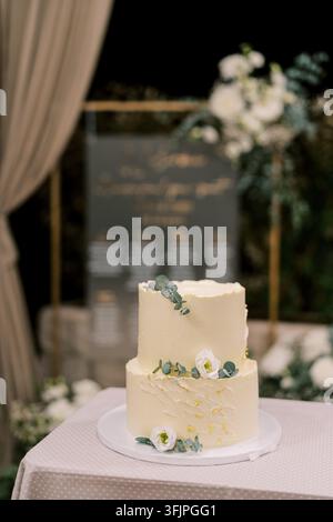 A two tier white wedding cake decorated with white lisianthus flowers and eucalyptus leaves, displayed on a table with a soft polka dot tablecloth at Stock Photo