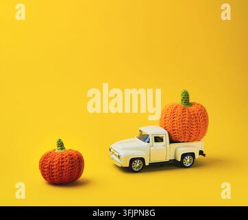 White truck is carrying two orange pumpkins. The scene is set on a yellow background. Scene is cheerful and playful, as the pumpkins and truck seem to Stock Photo