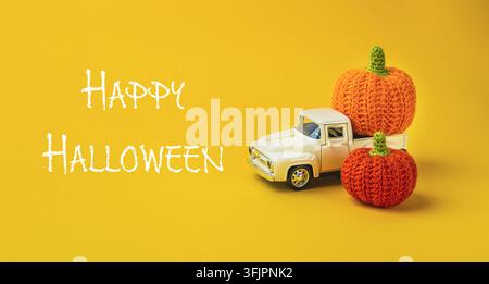 Toy truck positioned beside colorful knitted pumpkins on bright yellow backdrop, creating festive autumn atmosphere Stock Photo