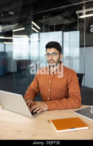 Professional businessman working on laptop at office desk, focused young man typing on computer for corporate project, digital workplace and business communication concept with notebook and documents. Stock Photo