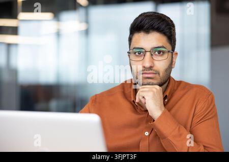 Professional businessman working on laptop in office, focused young man with glasses analyzing documents and financial data at his desk for corporate business strategy and development planning. Stock Photo