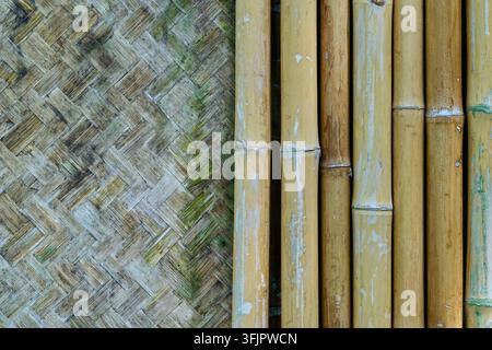 Close-up texture of traditional woven bamboo mat combined with vertical yellow bamboo stems background. Stock Photo