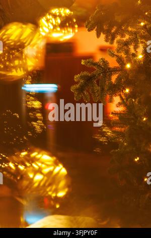 Selective focus on pine tree needles lit by yellow string lights alongside reflective glass baubles. Creates a cozy abstract holiday background filled Stock Photo
