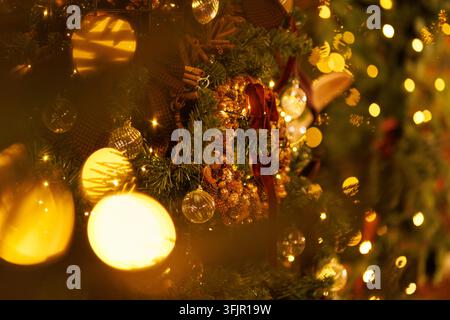 Atmospheric shot showing bright, out-of-focus golden light flares sweeping across a decorated Christmas tree with a pinecone wreath and hanging orname Stock Photo