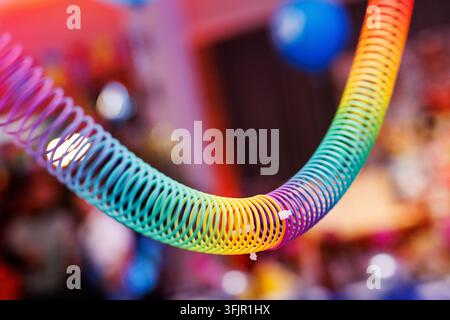 Close-up of a plastic rainbow spiral spring hanging indoors against a blurred background. Bright colors create a playful atmosphere at a celebration o Stock Photo