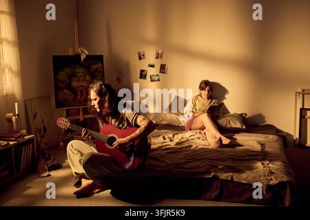 Couple Relaxing at Home with Man Playing Guitar in Bedroom Stock Photo