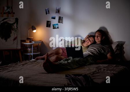 Couple Lying in Bed and Watching Movie on Laptop at Night Stock Photo