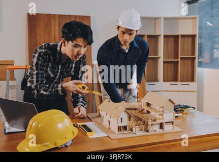 Asian architect and engineer team checking architectural house model using measuring tape on the table at office studio. Stock Photo