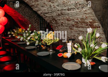 Elegant restaurant table setting with fresh fruit and white tulips in rustic brick interior Stock Photo