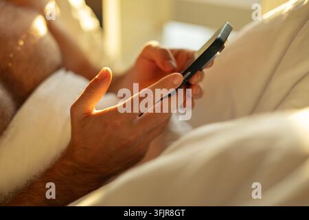 A man watches the news in the morning using a smartphone in bed. Stock Photo