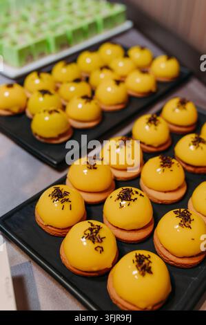 Yellow glazed pastries with chocolate sprinkles on black trays Stock Photo