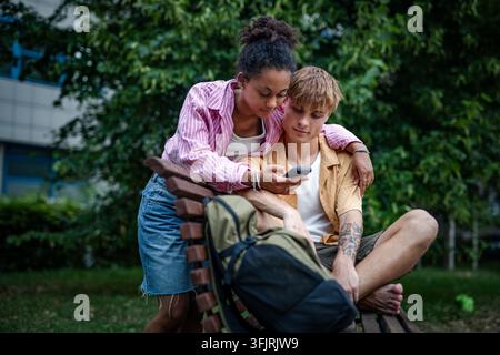 Young university students sitting on bench in park near college campus. Stock Photo