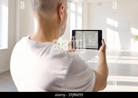 Back view of man using tablet to inspect bright interior room in sunny hall Stock Photo