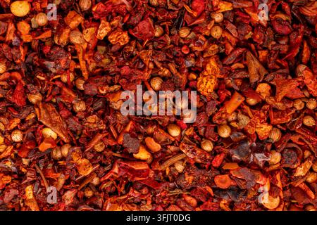 Spicy seasoning blend creating a vibrant red and orange food background, with various dried pepper pieces and whole coriander seeds offering a rich te Stock Photo
