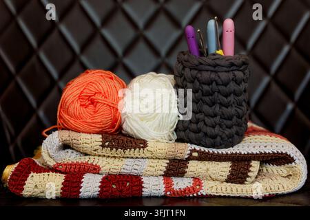 Orange and white yarn balls, crochet hooks and handmade knitting blanket. Concept for mental wellbeing, relax and hobby  Stock Photo