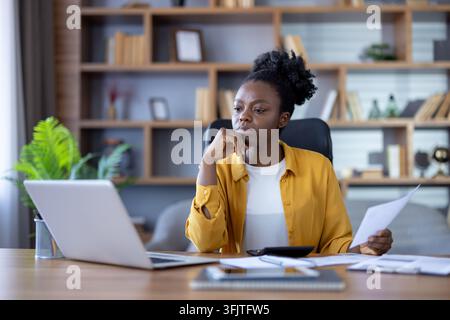 Businesswoman working on laptop and reviewing documents at desk, focused professional woman analyzing financial data in modern office for corporate project management and business strategy. Stock Photo