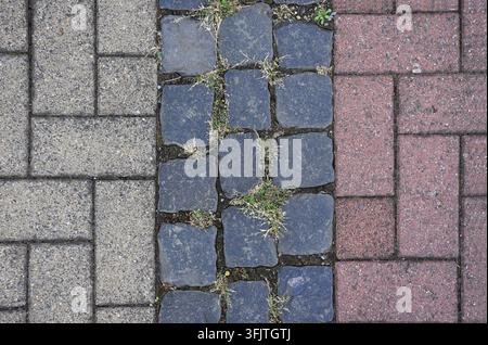 Close-up of cobblestone paths in three sections: grey, blue, and red. The beige and red sections feature rectangular bricks in a herringbone pattern. Stock Photo