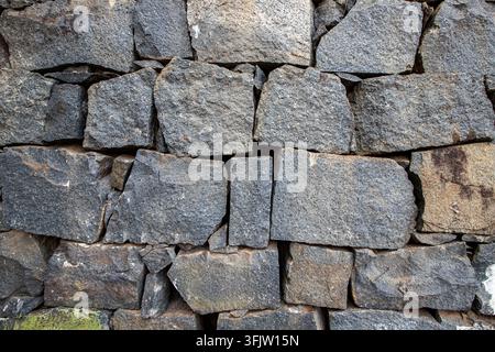 A detailed texture of stacked natural stone masonry showing the irregular shapes and weathered surfaces of hand cut granite blocks in a garden wall Stock Photo