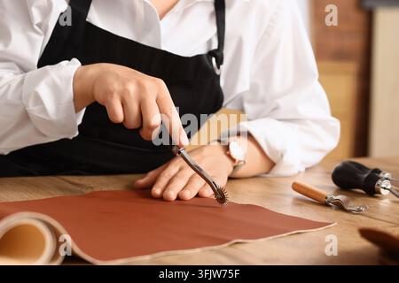 Leather craft and artisan workshop, skilled leatherworker using a tracing wheel to mark brown hide for custom handmade goods in a creative studio Stock Photo