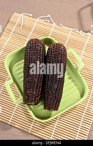 Two Black Purple Corn Cobs on Green Tray with Bamboo Mat Background Stock Photo