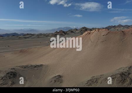 Rippled sand fills a broad desert valley framed by distant barren ranges under a bright sky. The soft dunes contrast with the rugged horizon. Stock Photo