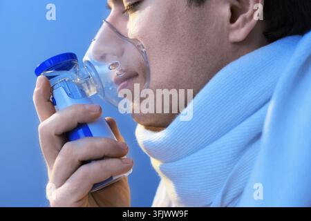 Man using inhaler mask for respiratory treatment during seasonal cold and flu illness. Concept of viral infection, asthma relief, recovery, and home h Stock Photo