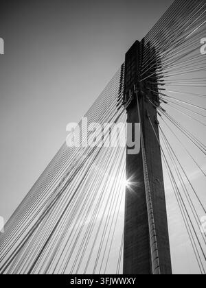 Black and white low angle abstract of Port Mann Bridge concrete tower steel cables and sun starburst in Surrey British Columbia. Stock Photo