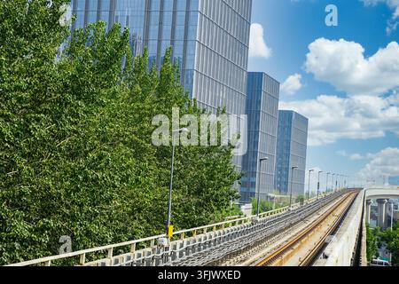 Elevated subway tracks running between urban high-rise buildings and green trees Stock Photo