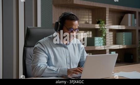 Motivated Indian business man in wireless headphones stretching hands before work on laptop indoor office listening music businessman male worker Stock Photo