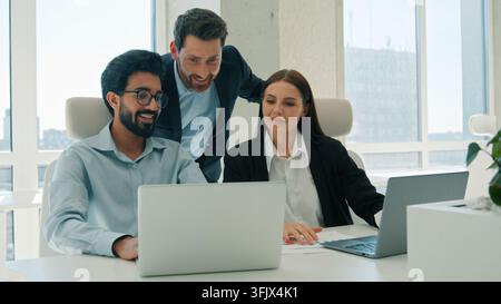 Happy business team working together in office smiling three coworkers discuss project results laptop ethnic businessmen businesswoman creative group Stock Photo