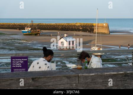 People relax during low tide at Folkestone Harbour, Kent, viewing the pink "Shelter in Place" art installation on the beach. Stock Photo