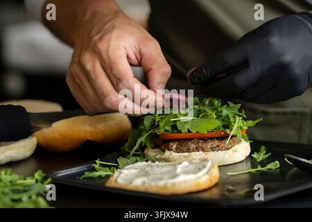 Beef burger being freshly assembled with a juicy beef patty, crisp arugula, tomato slices and pickled red onion on a soft bun. Stock Photo