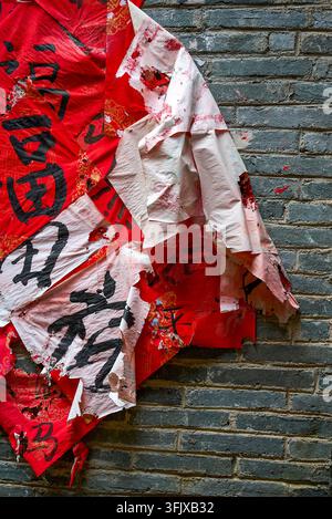 Close-up: the old house's gray brick walls are stained with torn and peeling red paper scraps, and the weathered walls show traces of time. Stock Photo