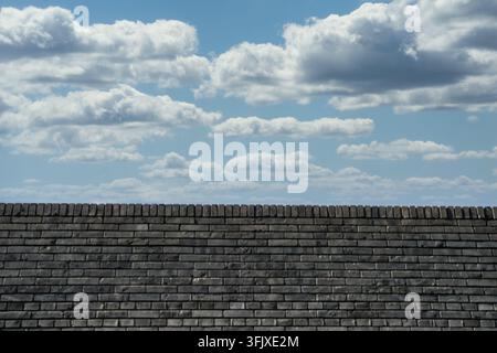 Symmetrical composition of weathered grey brick wall and layered white clouds Stock Photo