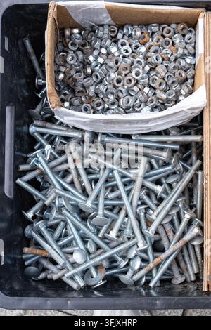 Metal bolts, nuts and fasteners collected in a container. Industrial hardware for construction, repair, manufacturing and technical work. Stock Photo