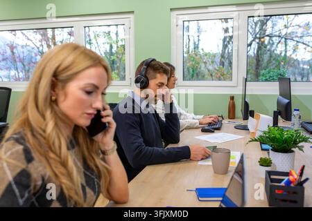 Diverse team of professionals collaborating and focusing on their tasks at a long desk in a contemporary office setting, featuring technology, communi Stock Photo