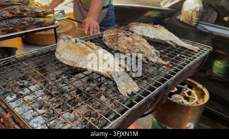 BANGKOK, THAILAND - MAR 15, 2026: Salt-crusted whole fish cooking on a charcoal barbecue grill at a street food stall in Bangkok, Thailand. Stock Photo
