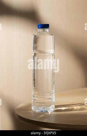 A clear bottle of water stands on a wooden table, illuminated by warm natural light with soft shadows, creating a clean and simple still life. Stock Photo